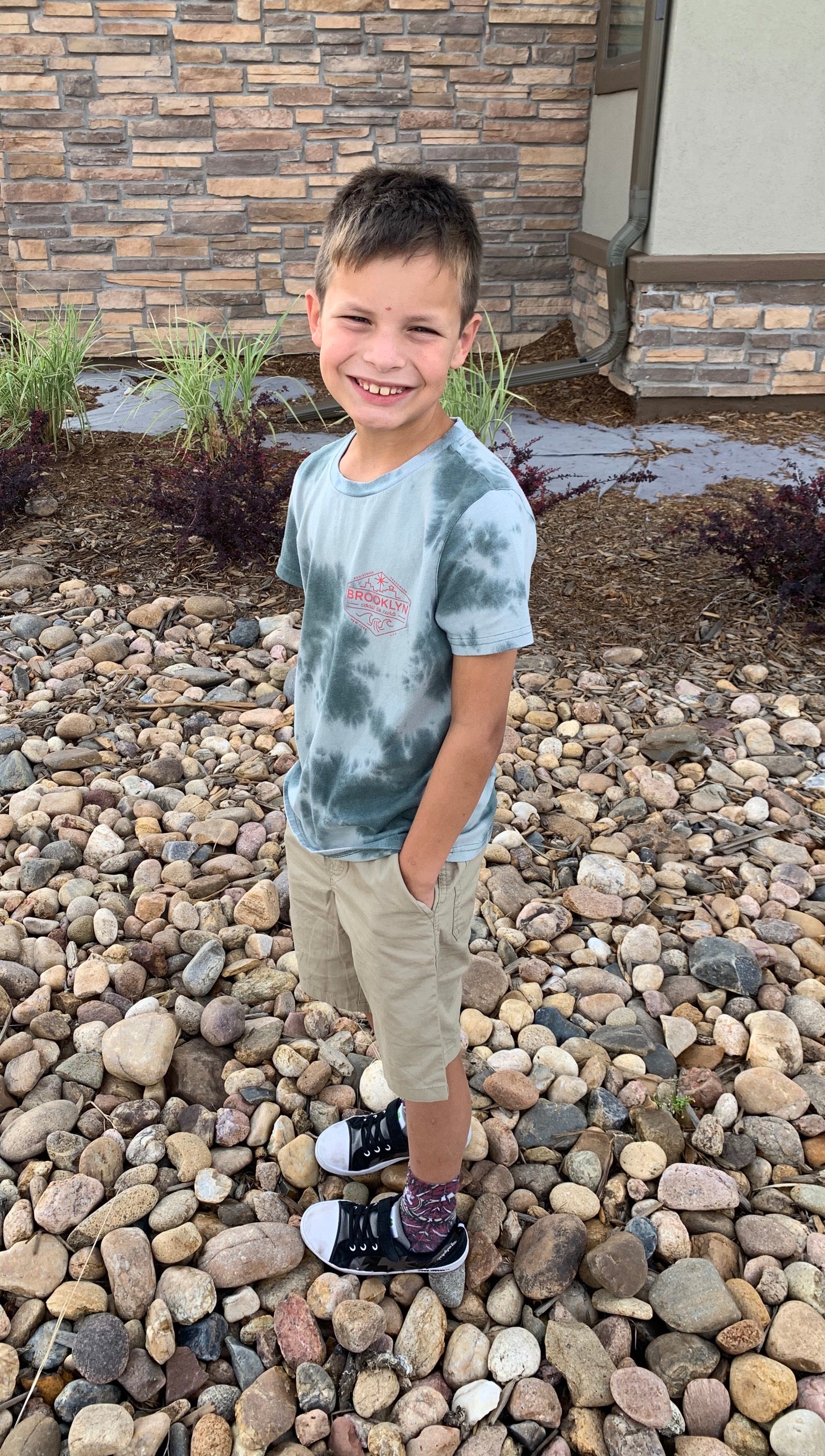Young boy standing on a rocky ground with a stone wall in the background