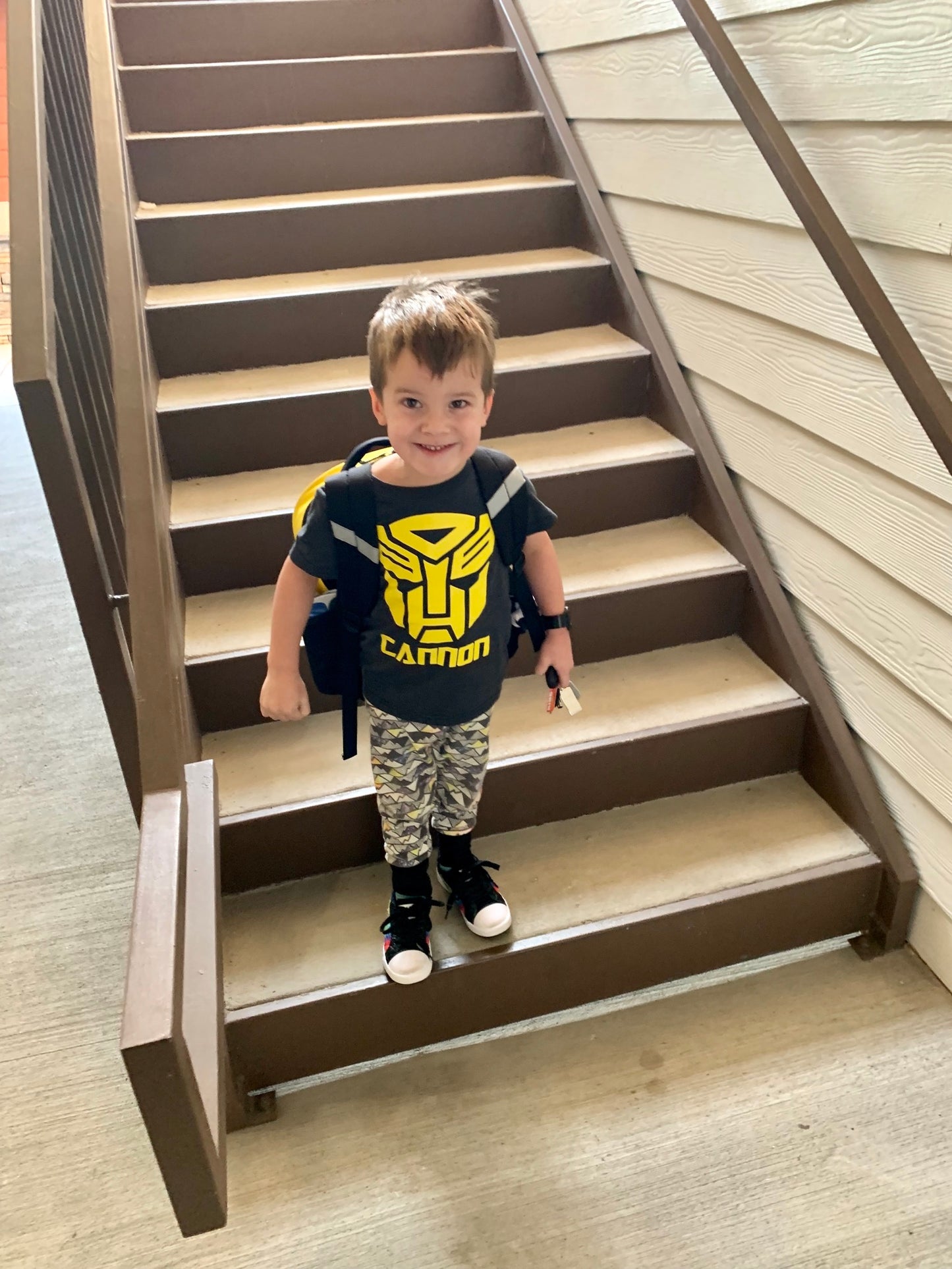 Child standing on a set of stairs wearing a shirt with a logo and text.
