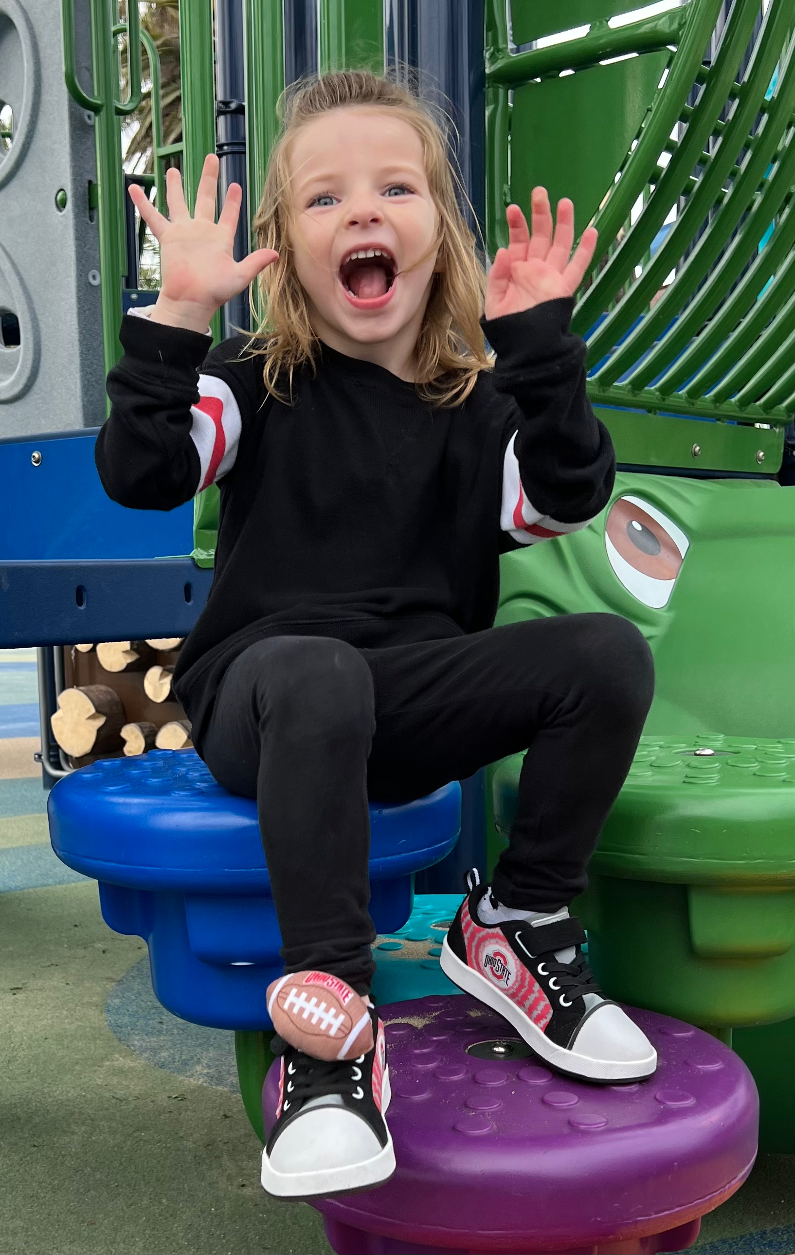 Child sitting on a playground swing set with arms raised