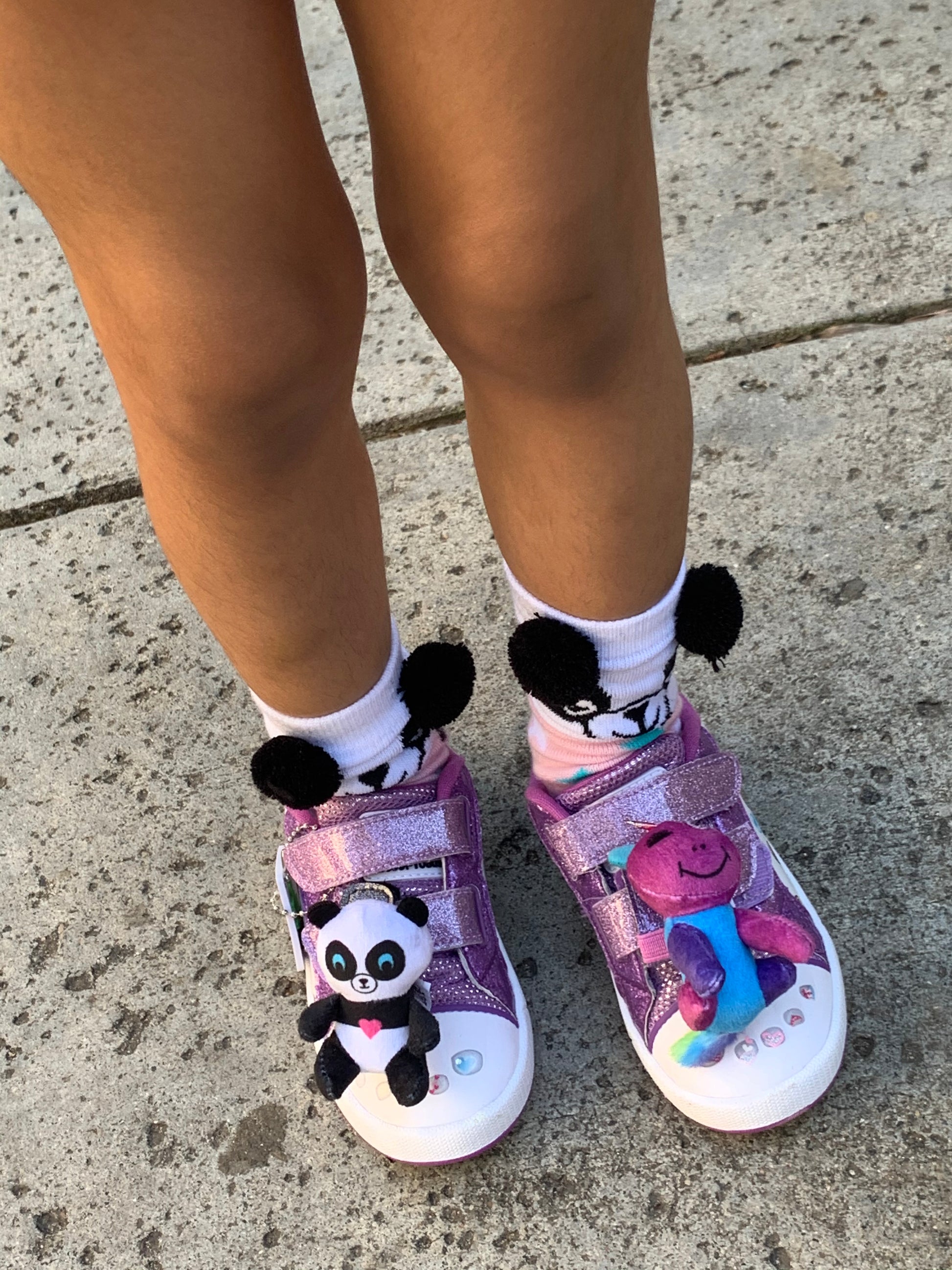 Children's shoes with panda design and pom-poms on a concrete surface